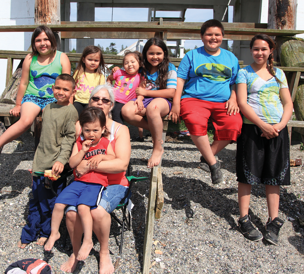 A group of Native kids and one Native elder smile at the camera.
