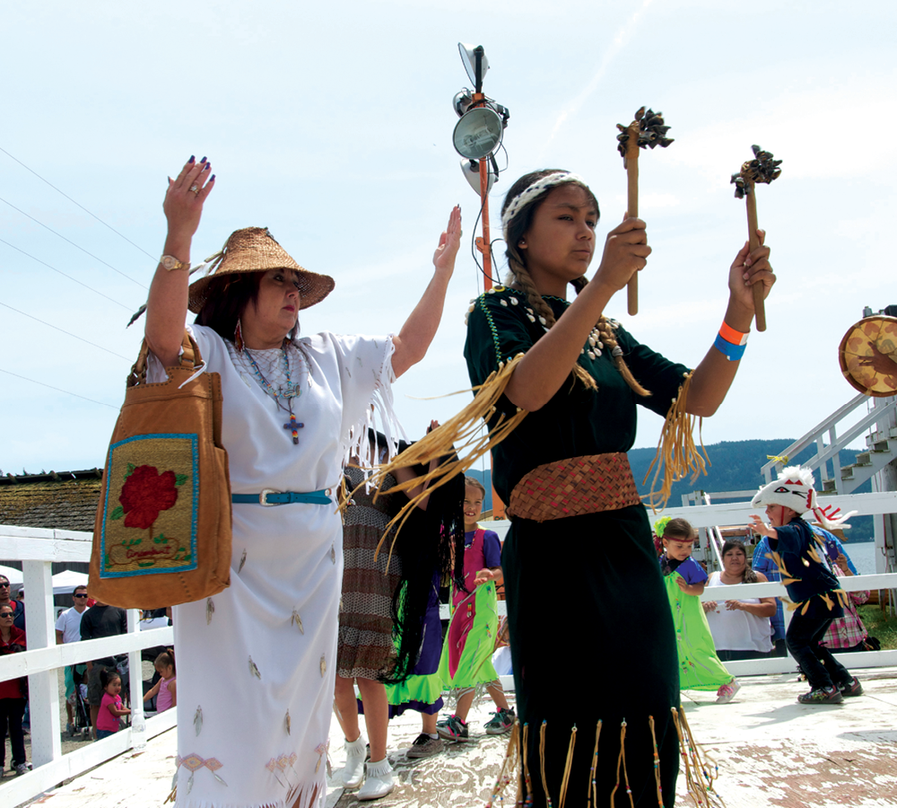 Lummi woman and girl with traditional garb lead a dance.