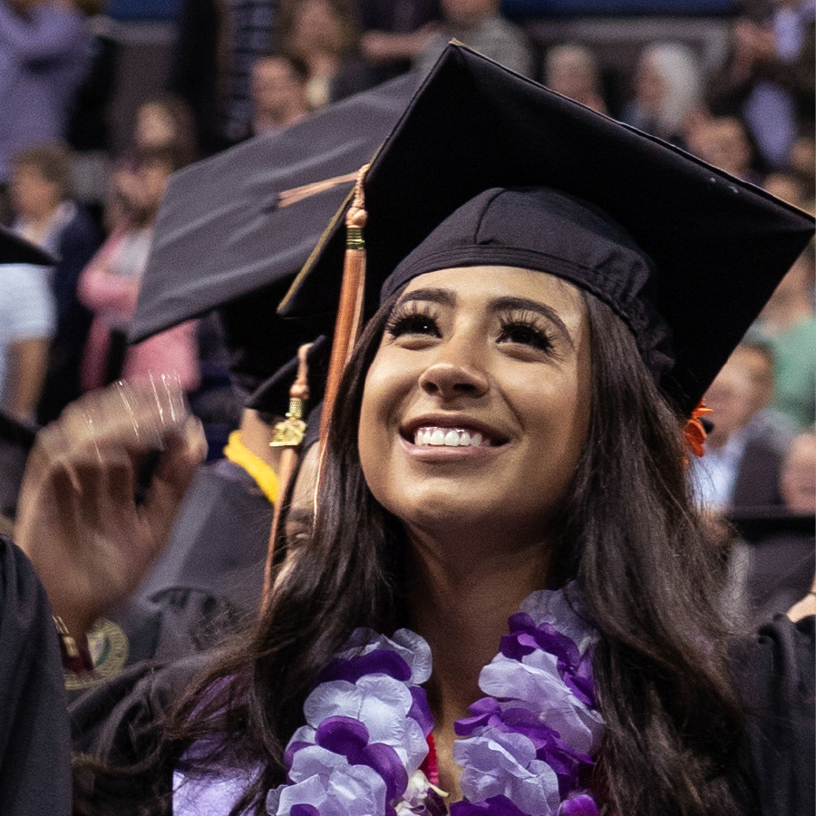 Photo of a young woman at University of Washington graduation wearing a cap and gown and purple lei
