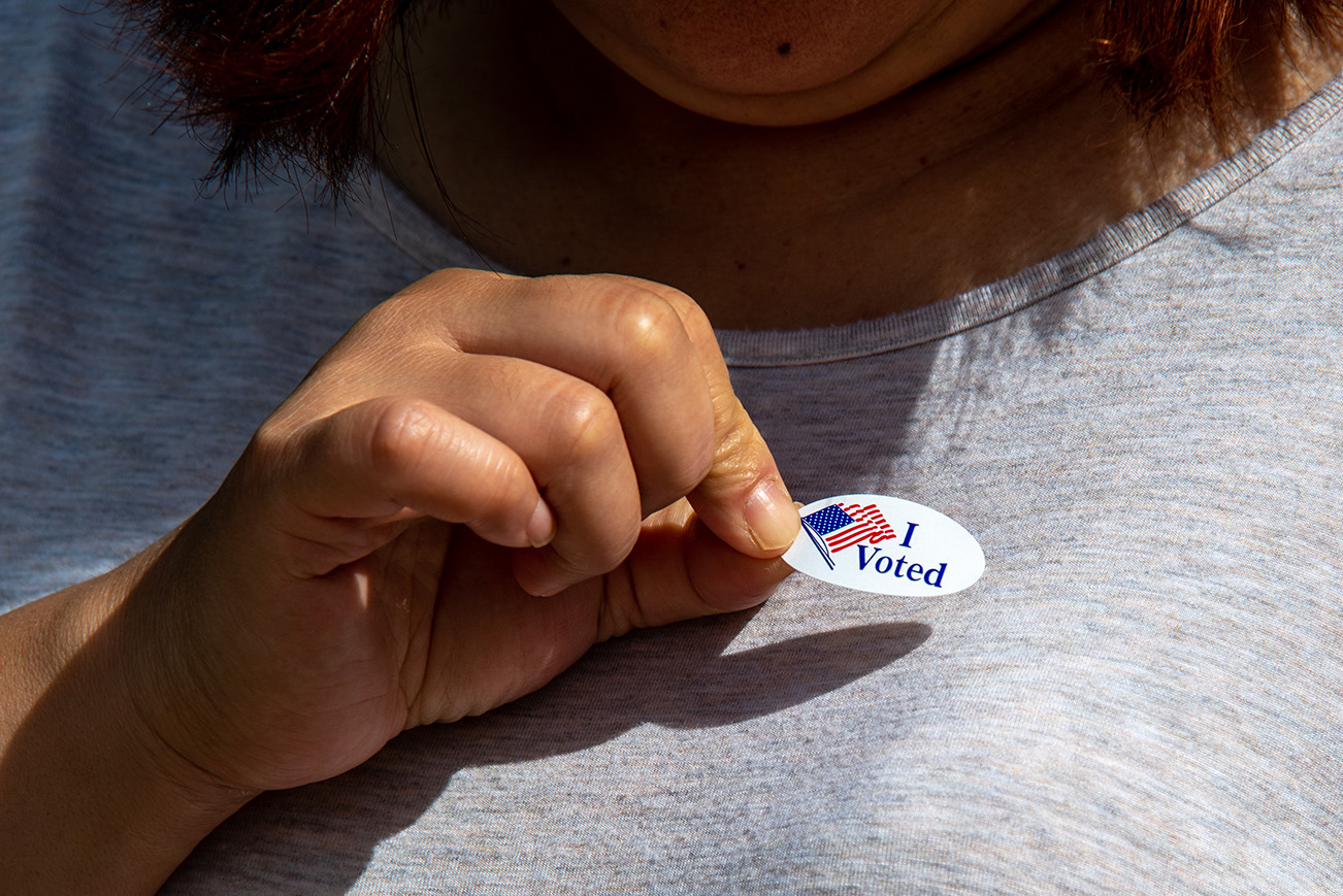 A close up of a person's chest, with a hand raised holding a white sticker that says 